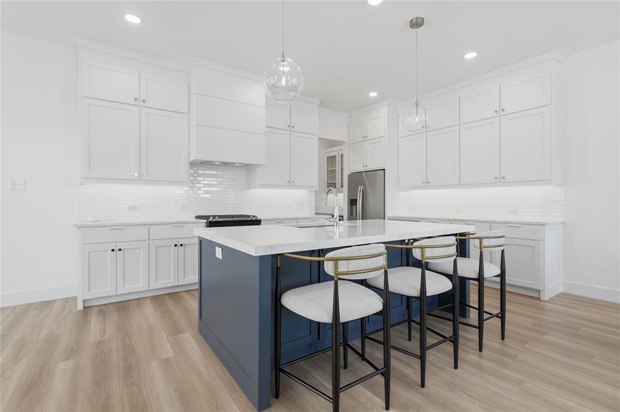 Kitchen featuring a spacious blue island with seating, white shaker cabinetry, white subway tile backsplash, light wood-finish flooring, and recessed lighting