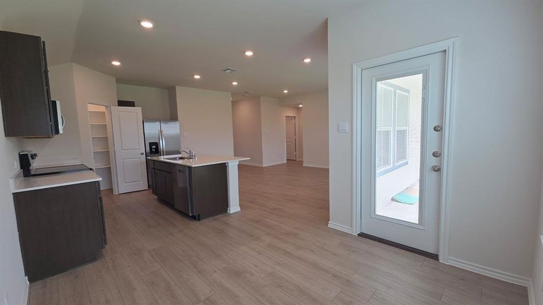 Open-concept kitchen featuring wood-finish flooring, recessed lighting, white countertops, a central island with an undermount sink, and stainless steel appliances Open-concept kitchen featuring wood-finish flooring, recessed lighting, white countertops, a central island with an undermount sink, and stainless steel appliances
