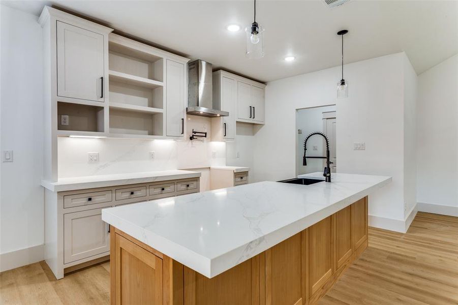 Kitchen with light wood-style floors, a center island with sink, wall chimney exhaust hood, light stone counters, and recessed lighting Kitchen with light wood-style floors, a center island with sink, wall chimney exhaust hood, light stone counters, and recessed lighting
