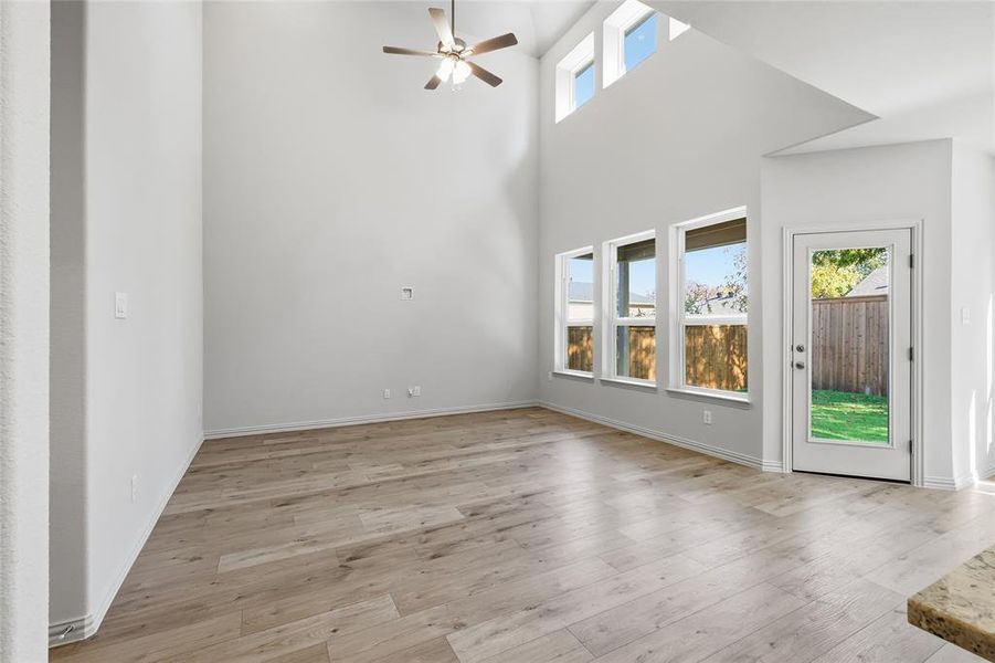 Unfurnished living room with light wood finished floors, ceiling fan, and a towering ceiling