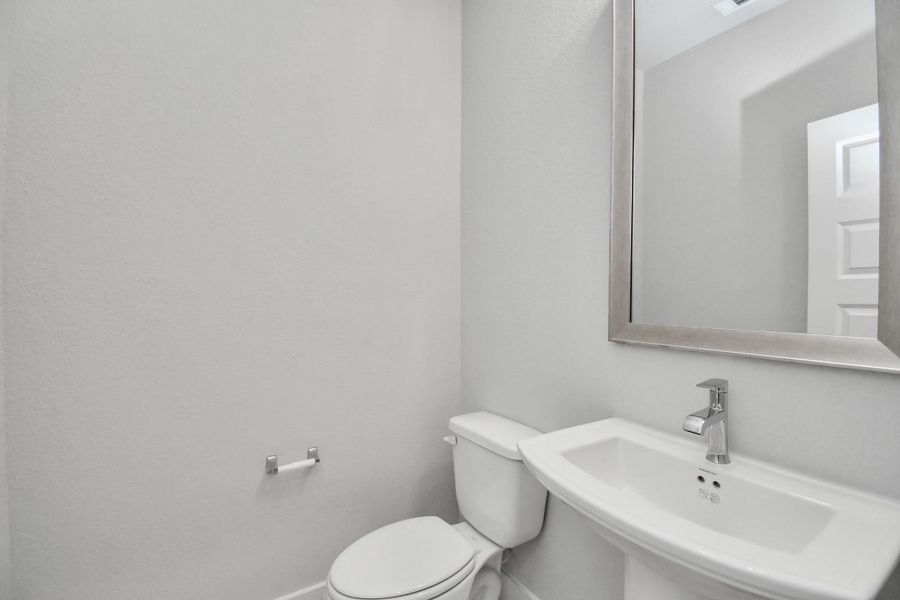 This half bathroom features a stylish pedestal sink, modern hardware, and bright recessed lighting, creating a sleek and inviting space. Sample photo of completed home with similar floor plan. Actual colors and selections may vary.