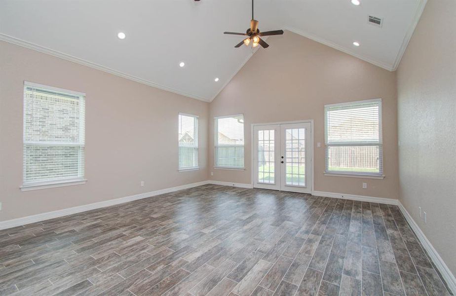 Spacious, airy living room with high ceiling, elegant wood-look tile flooring, ample natural light from multiple windows, and glass doors leading to the backyard.