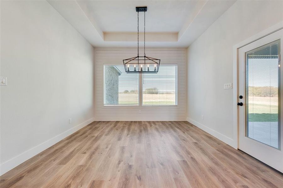 Unfurnished dining area featuring a chandelier, light hardwood / wood-style flooring, and a tray ceiling