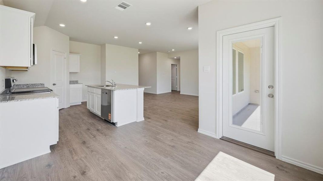 Kitchen featuring light stone countertops, range with electric stovetop, white cabinetry, recessed lighting, and a kitchen island with sink