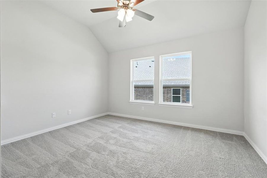 Empty room featuring light carpet, ceiling fan, and vaulted ceiling