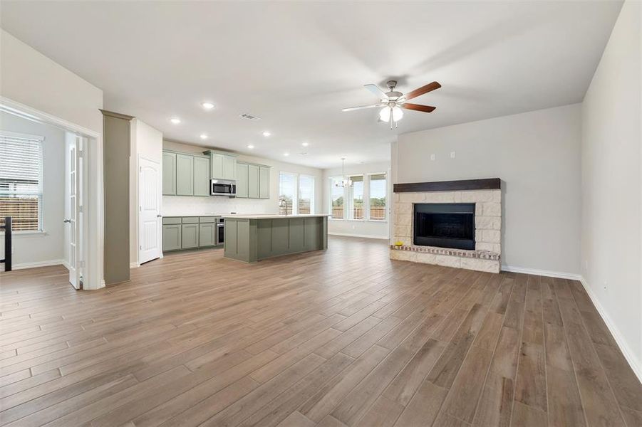 Unfurnished living room featuring recessed lighting, a ceiling fan, dark wood finished floors, a stone fireplace, and a chandelier Unfurnished living room featuring recessed lighting, a ceiling fan, dark wood finished floors, a stone fireplace, and a chandelier