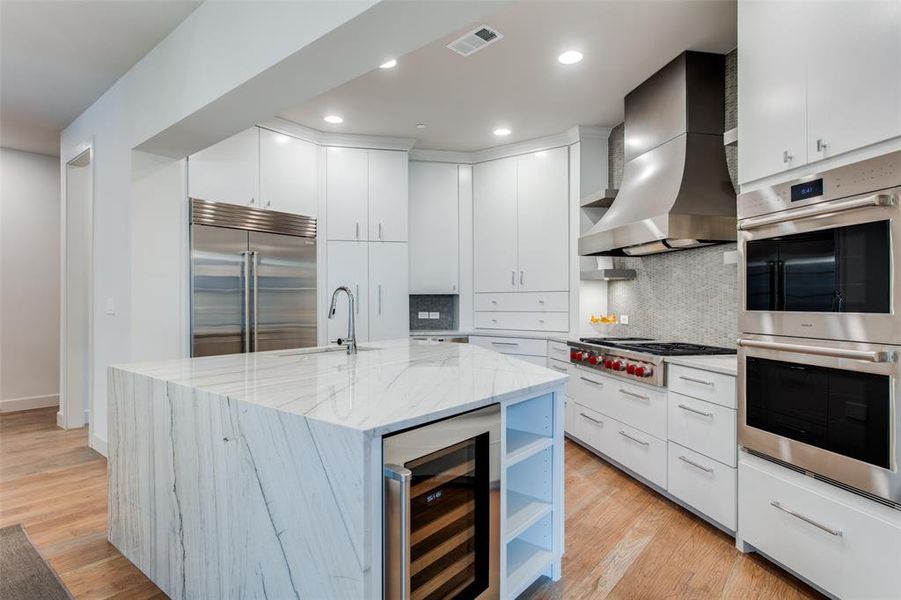 Kitchen with appliances with stainless steel finishes, light hardwood / wood-style flooring, tasteful backsplash, wine cooler, and wall chimney exhaust hood