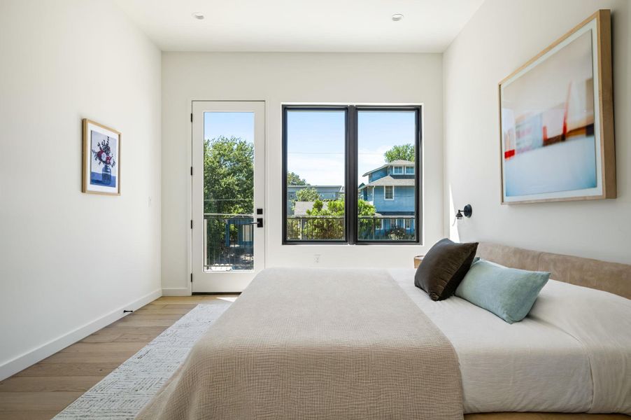 Natural light streams through large windows onto beautiful hardwood floors in this peaceful bedroom.