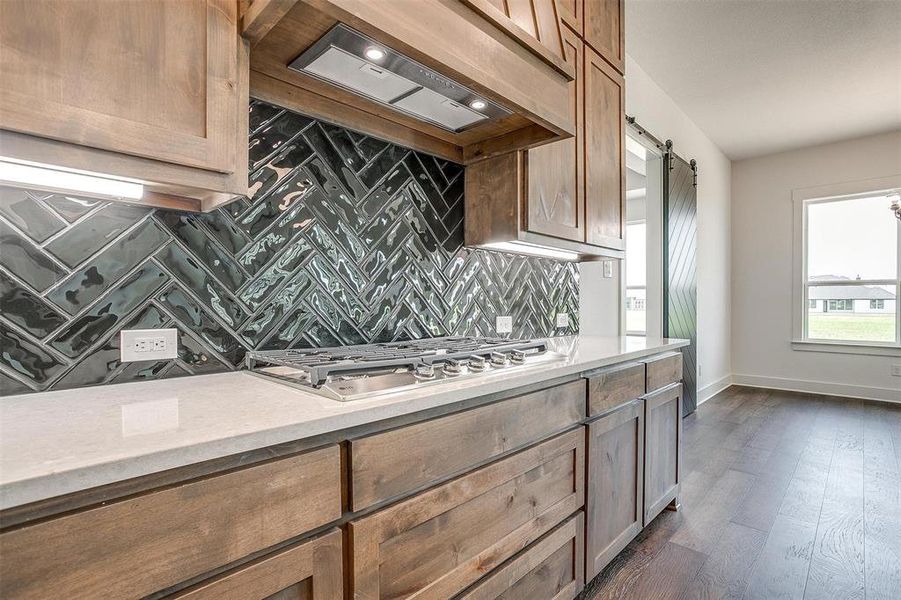 Kitchen with tasteful backsplash, stainless steel gas stovetop, a barn door, dark hardwood / wood-style floors, and custom range hood