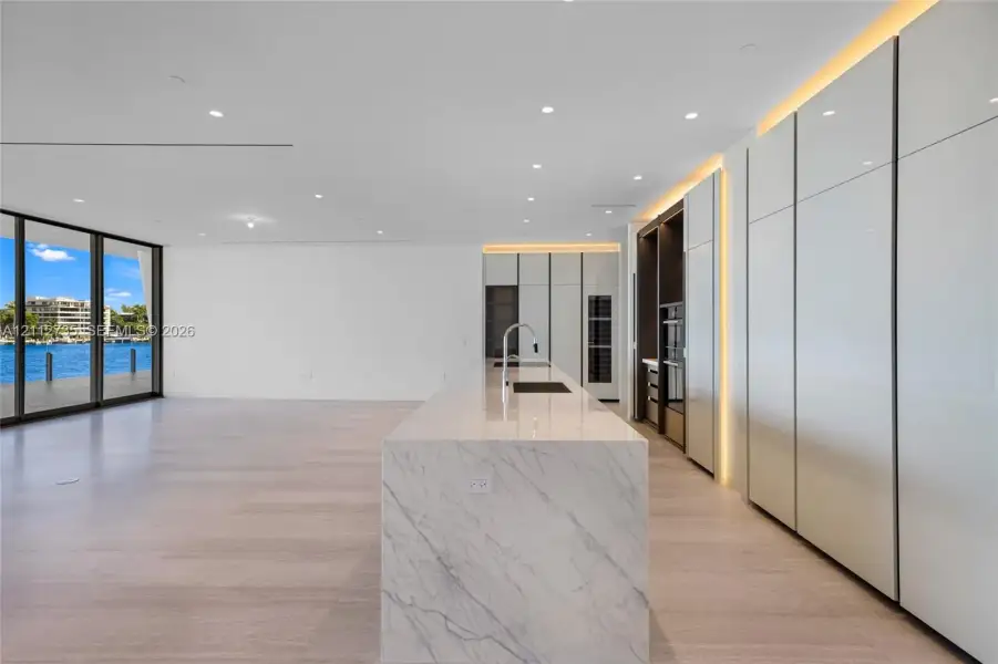 Kitchen featuring a stone-surface island, floor-to-ceiling high-gloss cabinetry, integrated lighting, wood-finish flooring, and expansive glass sliding doors