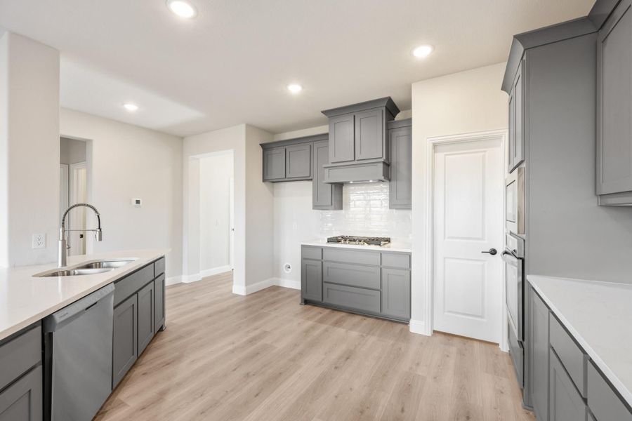 Kitchen with gray cabinets, white countertops, stainless sink, and light hardwood floors Kitchen with gray cabinets, white countertops, stainless sink, and light hardwood floors
