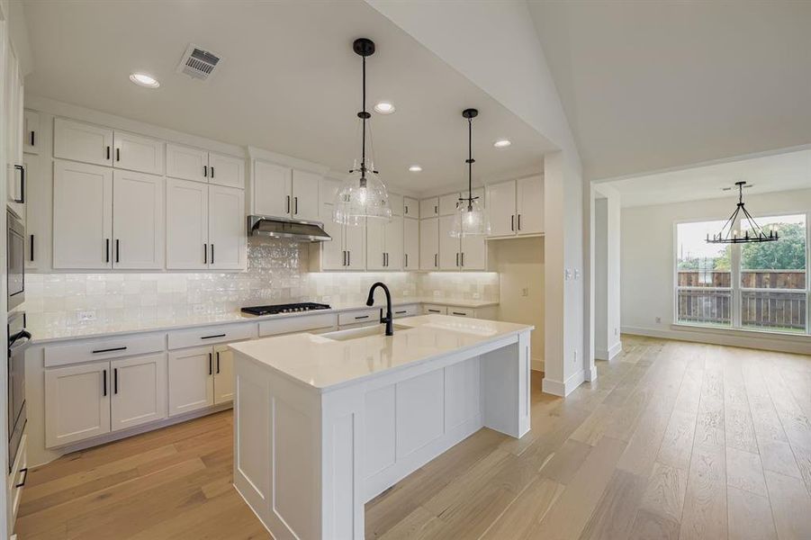 Kitchen featuring hanging light fixtures, tasteful backsplash, a kitchen island with sink, light wood-type flooring, and recessed lighting Kitchen featuring hanging light fixtures, tasteful backsplash, a kitchen island with sink, light wood-type flooring, and recessed lighting
