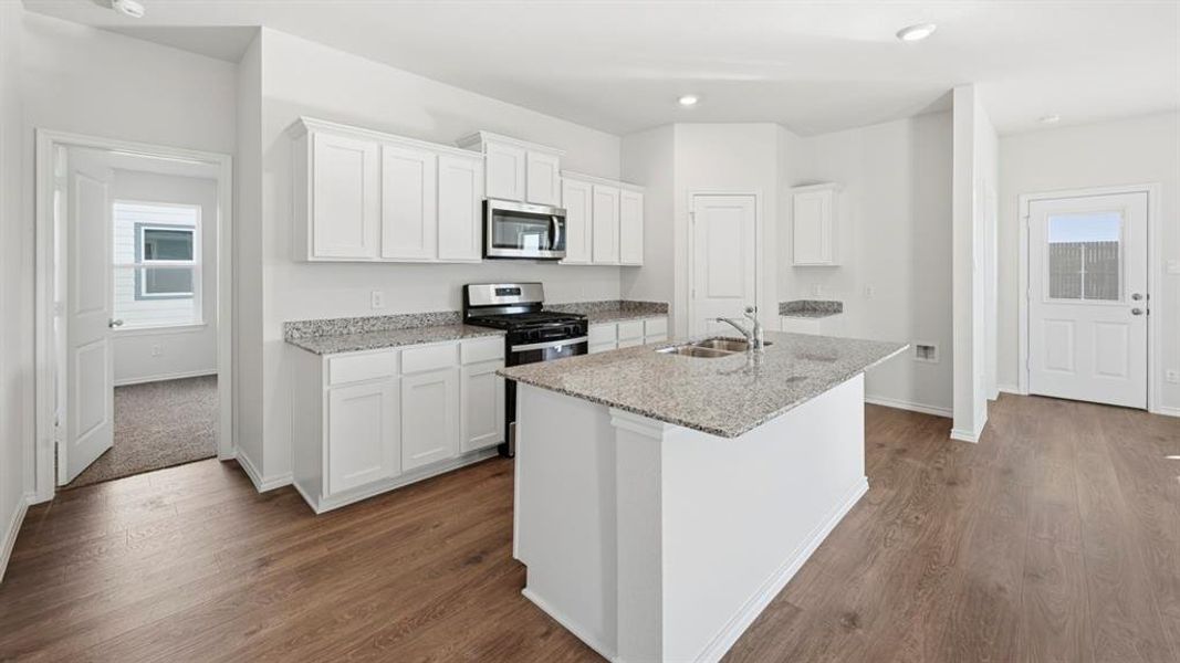 Kitchen featuring white cabinetry, light stone countertops, a center island with sink, stainless steel appliances, and dark wood finished floors Kitchen featuring white cabinetry, light stone countertops, a center island with sink, stainless steel appliances, and dark wood finished floors