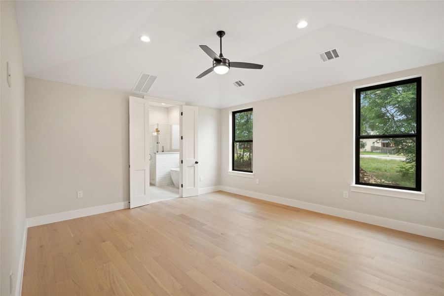 A spacious bedroom with light hardwood flooring opens to an adjoining private bathroom. A spacious bedroom with light hardwood flooring opens to an adjoining private bathroom.