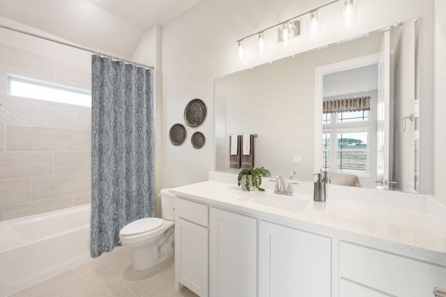 Bathroom with white vanity, quartz countertop, large mirror, and tub with tiled surround and blue curtain