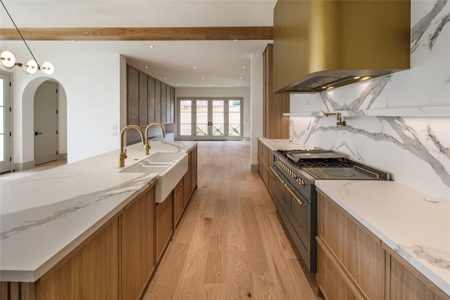 The closer you look, the better it gets. A statement range, brass pot filler, oversized brass hood, double faucets, and richly veined surfaces prove this kitchen wasn't designed from a standard finish package.