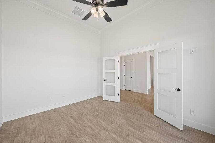 Spare room featuring light wood-type flooring, ceiling fan, a high ceiling, and ornamental molding