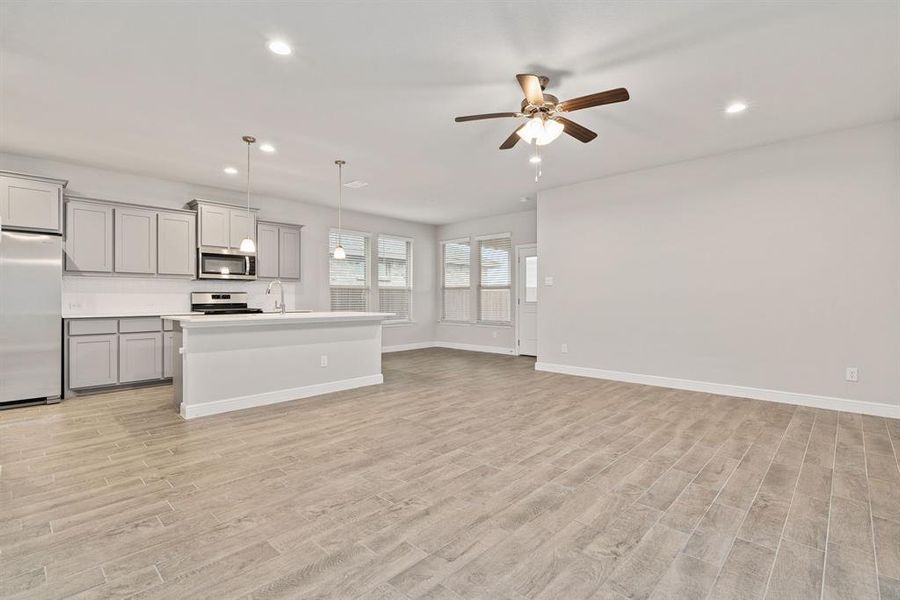 Kitchen with gray cabinetry, appliances with stainless steel finishes, a kitchen island with sink, pendant lighting, and light hardwood / wood-style floors