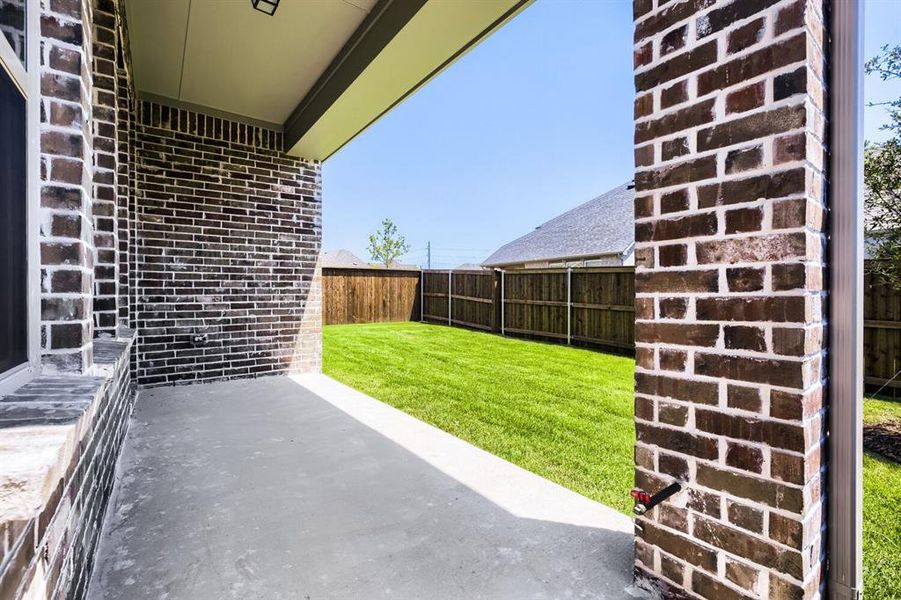 Covered patio with a concrete surface, a dark brick exterior, and a manicured lawn