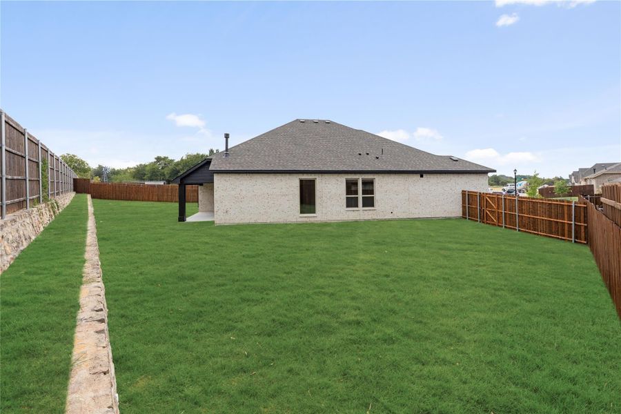 Backyard of single-story brick home with large lawn, covered patio, and wood privacy fence Backyard of single-story brick home with large lawn, covered patio, and wood privacy fence
