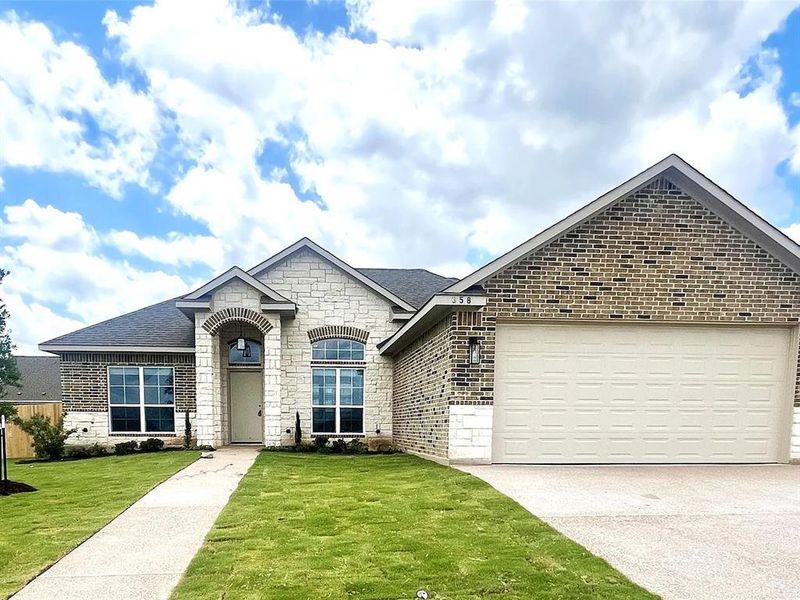Stone and brick facade home featuring an arched entry, a two-car garage, and a concrete pathway Stone and brick facade home featuring an arched entry, a two-car garage, and a concrete pathway