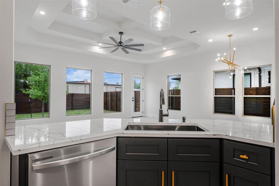 Modern kitchen featuring a dishwasher, stainless steel sink, recessed lighting, light stone countertops, and an elegant coffered ceiling. Modern kitchen featuring a dishwasher, stainless steel sink, recessed lighting, light stone countertops, and an elegant coffered ceiling.