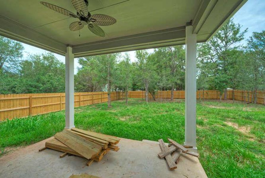 Fenced backyard featuring a ceiling fan, a patio area, and view of wooded area