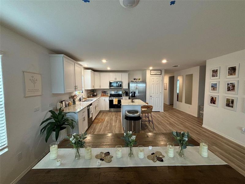 Kitchen featuring appliances with stainless steel finishes, a center island, white cabinets, light wood-type flooring, and light stone counters
