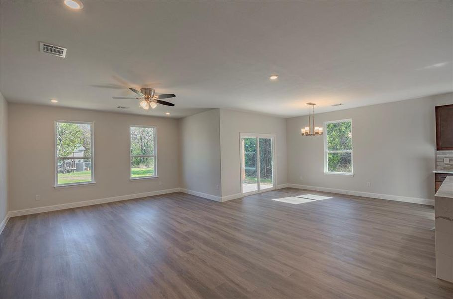 Unfurnished living room with hardwood / wood-style flooring, ceiling fan with notable chandelier, and plenty of natural light