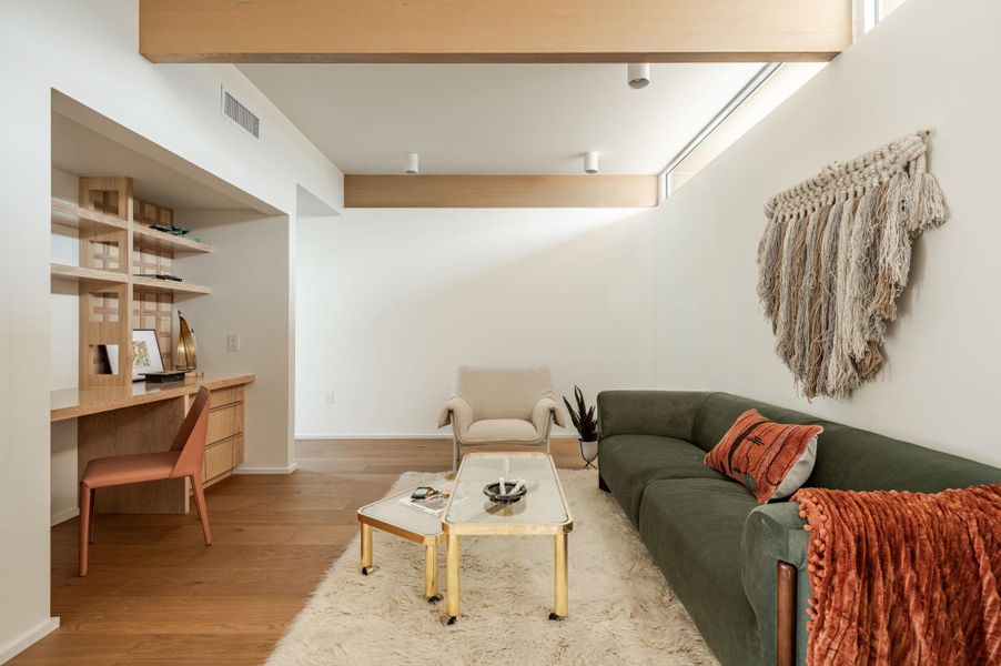 Living area with built in study area, light wood-style floors, and beamed ceiling