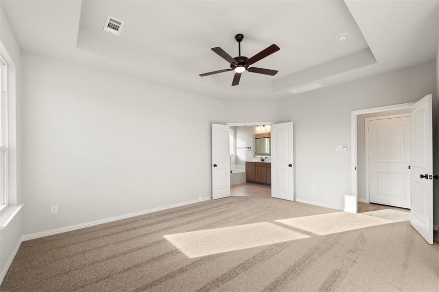 Unfurnished bedroom featuring a tray ceiling, light colored carpet, ensuite bathroom, and a ceiling fan Unfurnished bedroom featuring a tray ceiling, light colored carpet, ensuite bathroom, and a ceiling fan