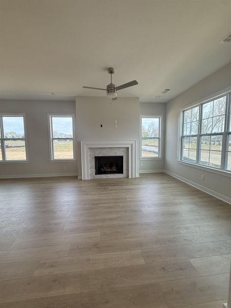 Unfurnished living room with a fireplace, ceiling fan, and light wood-style flooring