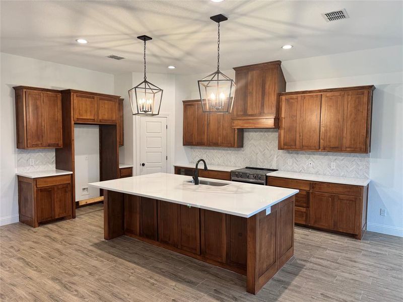 Kitchen with sink, stainless steel range with electric cooktop, hanging light fixtures, a center island with sink, and light wood-type flooring