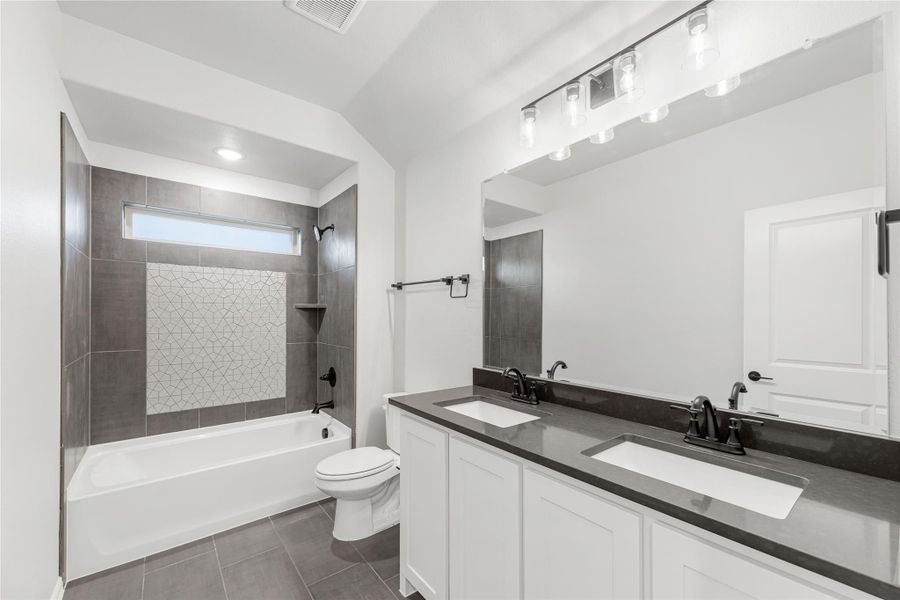 Bathroom with double sink vanity, dark countertop, soaking tub, and gray tile shower surround