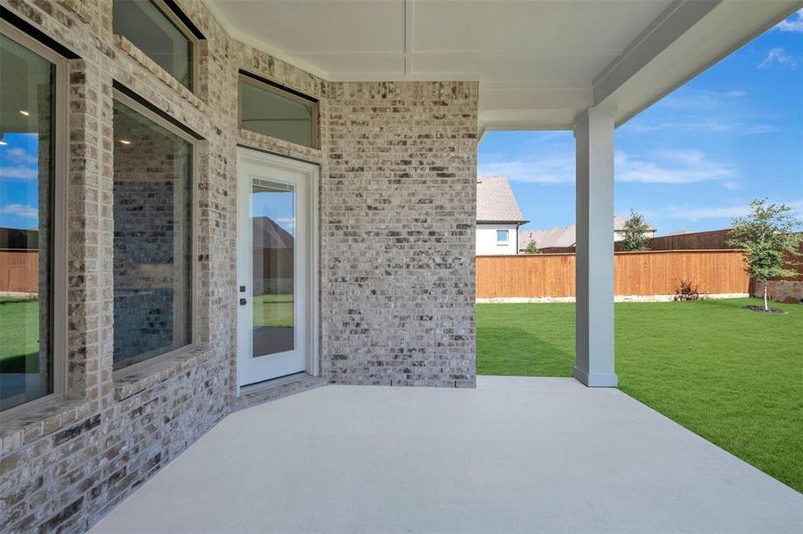 Expansive covered patio featuring a concrete surface, white support columns, and a brick exterior facade Expansive covered patio featuring a concrete surface, white support columns, and a brick exterior facade