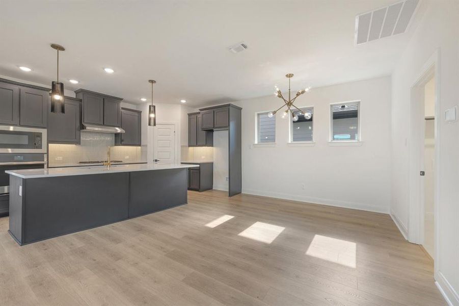Open-concept kitchen and dining area featuring dark gray cabinetry, stainless steel appliances, a center island with pendant lighting, and wood-finish flooring