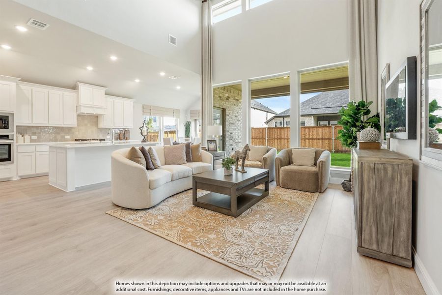 Open-concept living room with two-story ceiling, hardwood floors, and white kitchen visible in background Open-concept living room with two-story ceiling, hardwood floors, and white kitchen visible in background