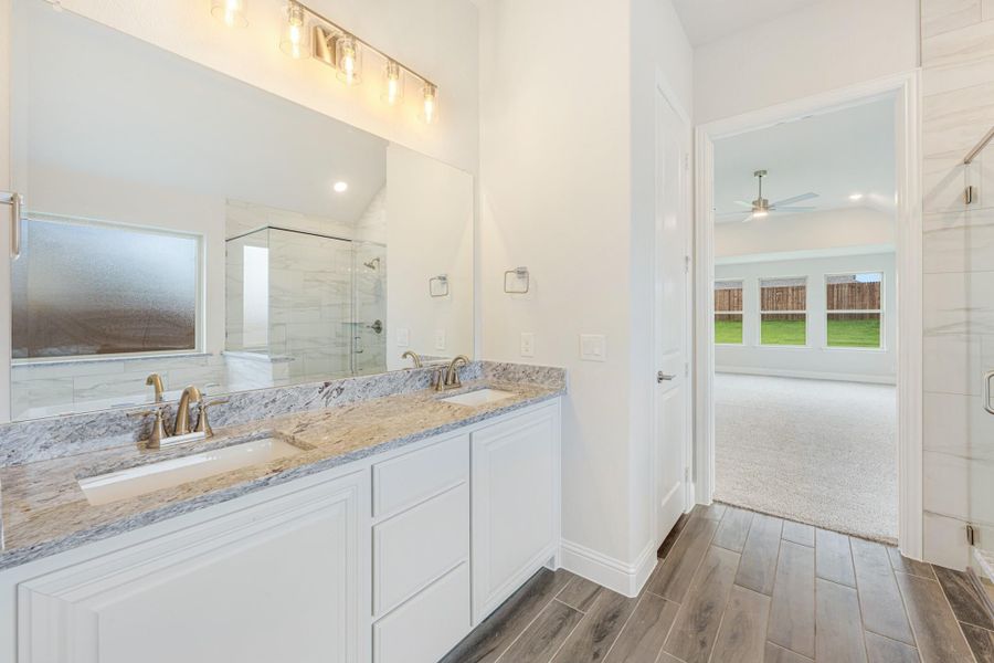 Master bathroom with double vanity, granite countertops, white cabinets, and glass shower visible in mirror reflection