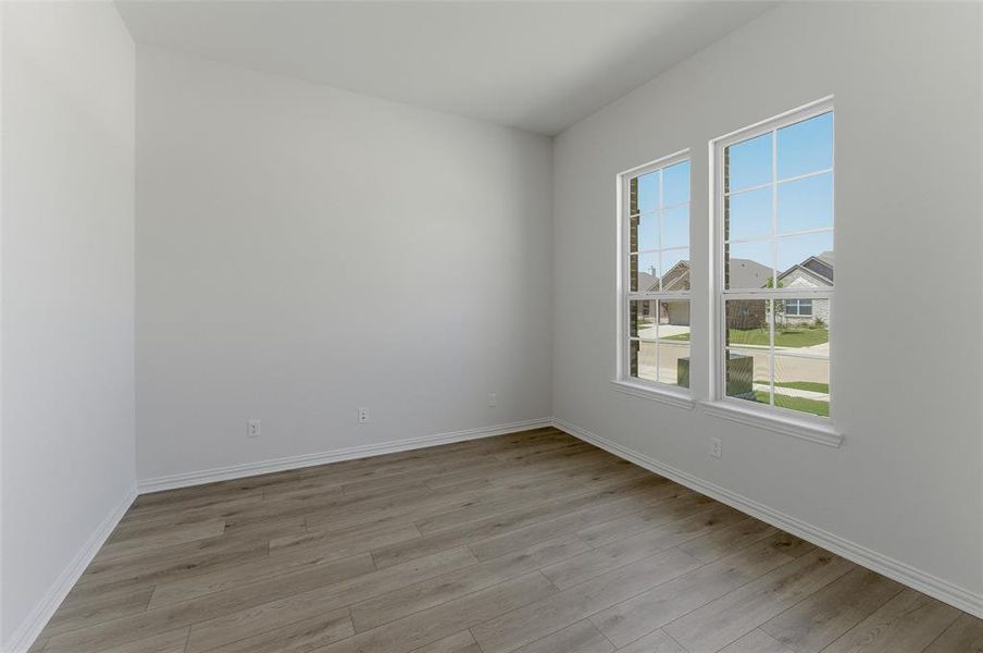 Spacious room featuring wood-finish flooring, two large windows with grid patterns, bright white walls, white baseboards, and multiple electrical outlets Spacious room featuring wood-finish flooring, two large windows with grid patterns, bright white walls, white baseboards, and multiple electrical outlets