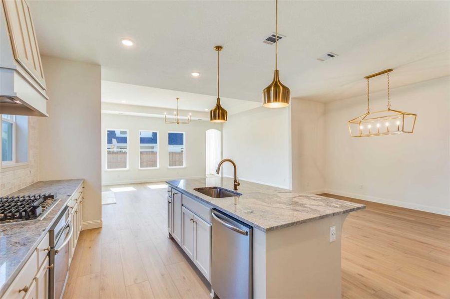 Kitchen with appliances with stainless steel finishes, an island with sink, decorative light fixtures, and sink