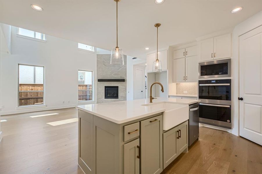 Kitchen featuring light hardwood / wood-style floors, a kitchen island with sink, a premium fireplace, hanging light fixtures, and decorative backsplash