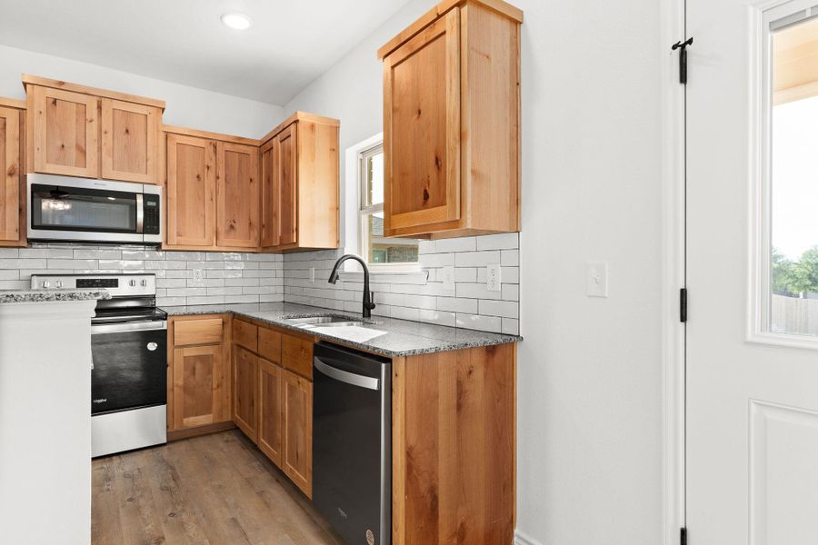 Kitchen featuring a sink, appliances with stainless steel finishes, backsplash, light wood-style flooring, and stone countertops Kitchen featuring a sink, appliances with stainless steel finishes, backsplash, light wood-style flooring, and stone countertops