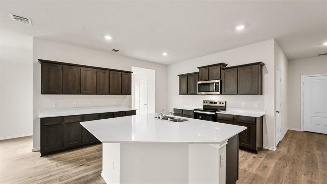 Spacious kitchen featuring an expansive island with a double basin sink, dark wood cabinetry, and light countertops Spacious kitchen featuring an expansive island with a double basin sink, dark wood cabinetry, and light countertops