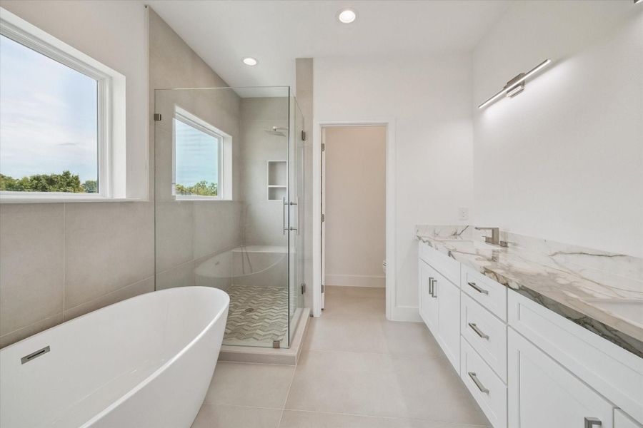 Spa-inspired finishes elevate this impressive primary bathroom, where a freestanding soaking tub sits beside a spacious glass-enclosed walk-in shower. Large-format neutral tile creates a calm, sophisticated backdrop, while the shower features built-in niches, a rainfall-style fixture, and decorative patterned flooring. A long white vanity with dramatic stone-look countertops provides generous storage and prep space, completing a luxurious retreat designed for both function and relaxation. Spa-inspired finishes elevate this impressive primary bathroom, where a freestanding soaking tub sits beside a spacious glass-enclosed walk-in shower. Large-format neutral tile creates a calm, sophisticated backdrop, while the shower features built-in niches, a rainfall-style fixture, and decorative patterned flooring. A long white vanity with dramatic stone-look countertops provides generous storage and prep space, completing a luxurious retreat designed for both function and relaxation.