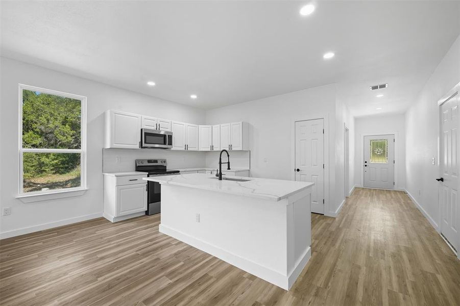 Kitchen featuring appliances with stainless steel finishes, white cabinets, a kitchen island with sink, recessed lighting, and light wood-style floors Kitchen featuring appliances with stainless steel finishes, white cabinets, a kitchen island with sink, recessed lighting, and light wood-style floors