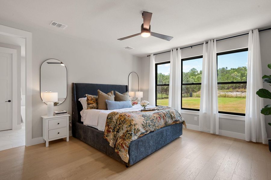 Natural light floods this peaceful bedroom featuring warm hardwood flooring and large picture windows.