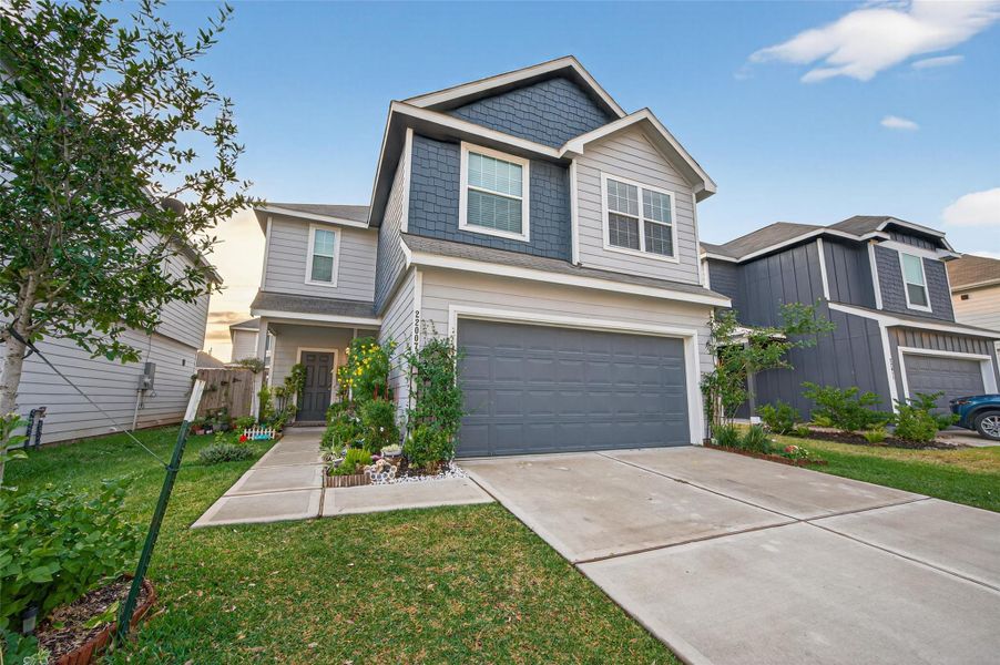 This photo showcases a modern two-story home with a gray exterior and a neatly maintained front yard. It features a spacious driveway leading to a two-car garage, and the entrance is accentuated by landscaped greenery.