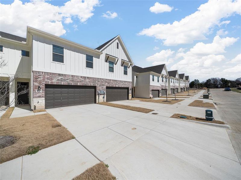 View of front facade featuring brick siding, concrete driveway, board and batten siding, a garage, and a residential view