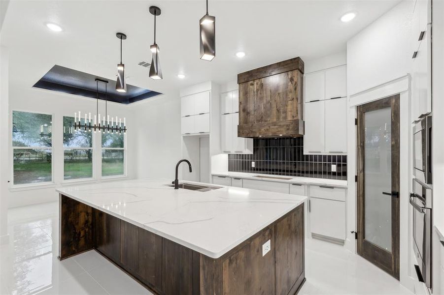 Kitchen with a kitchen island with sink, white cabinetry, sink, and decorative light fixtures