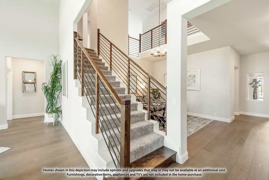 Carpeted staircase with wood and metal railing in a two-story foyer with hardwood floors and high ceilings
